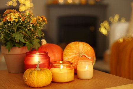 Burning candles, pumpkins and flowers on wooden table indoors. Autumn atmosphereの写真素材