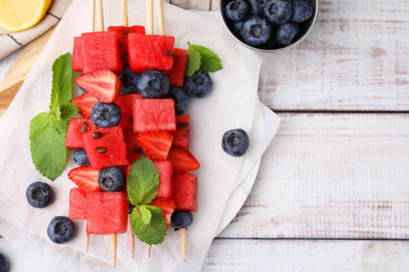 Skewers with tasty watermelon, strawberries, blueberries and mint on light wooden table, flat lay. Space for textの写真素材