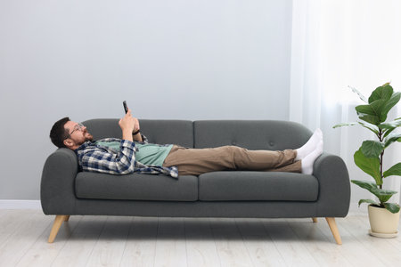 Smiling man with smartphone relaxing on sofa at homeの写真素材