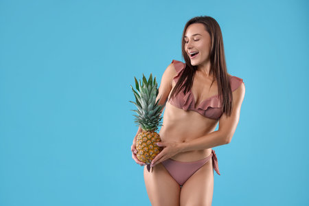 Woman in bikini with fresh pineapple on light blue background, space for textの写真素材