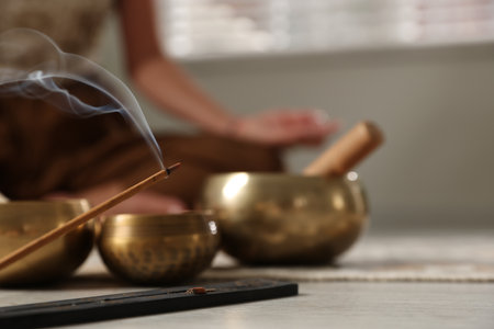 Incense stick smoldering in holder and tibetan singing bowls on floor, selective focus. Space for textの写真素材