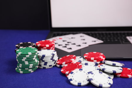 Laptop, poker chips and playing cards on blue table, closeup. Online game