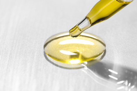 Cosmetic oil dripping from pipette on light gray background, closeup