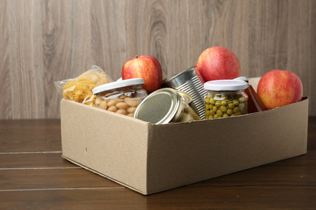 Different food products for donation in box on wooden table