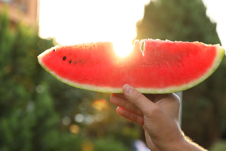 Man holding slice of juicy watermelon outdoors on sunny day, closeupの写真素材