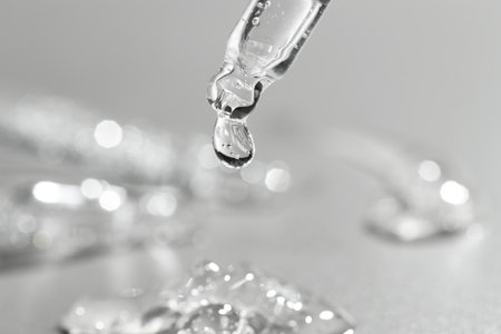 Dripping cosmetic serum from pipette on gray background, closeupの写真素材