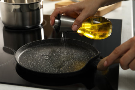 Woman pouring oil into frying pan on cooktop in kitchen, closeupの写真素材