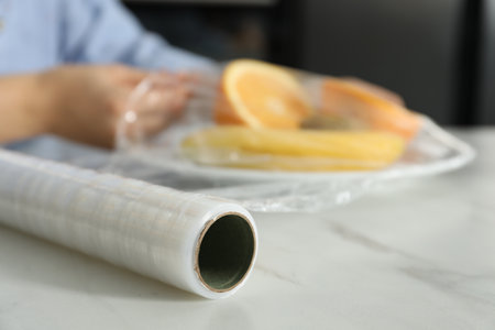 Woman putting plastic food wrap over plate with fruits at countertop in kitchen, selective focusの写真素材