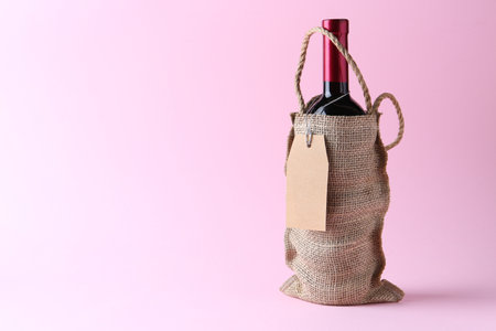 Wine bottle in burlap bag on pink background. Space for textの写真素材