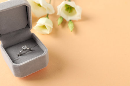 Beautiful ring with gemstone in box and flowers on beige background, closeup. Space for textの写真素材