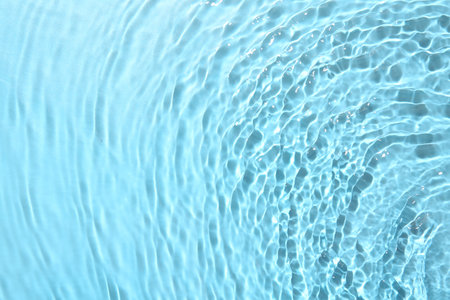 Rippled surface of clear water on light blue background, closeup