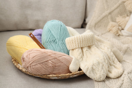 Skeins of soft yarn, crochet hooks and mittens on sofaの写真素材
