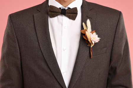 Groom in suit with stylish boutonniere on pink background, closeup