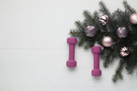 Dumbbells, fir tree branches and Christmas baubles on white table, flat lay. Space for textの写真素材