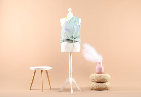Mannequin with cloth, measuring tape, vase and stool on beige backgroundの写真素材