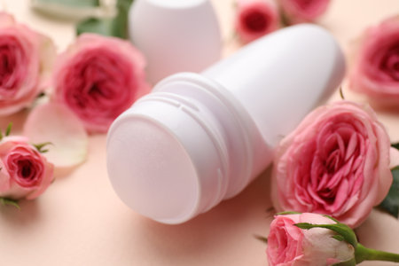 Roll-on deodorant and beautiful rose flowers on beige background, closeup