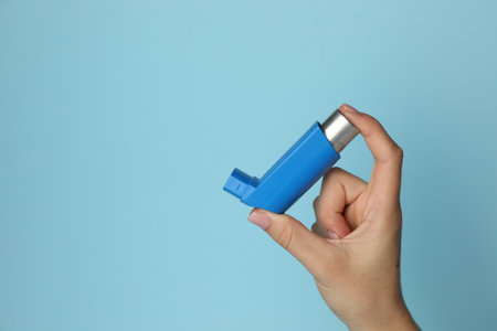 Woman holding asthma inhaler on light blue background, closeup. Space for textの写真素材
