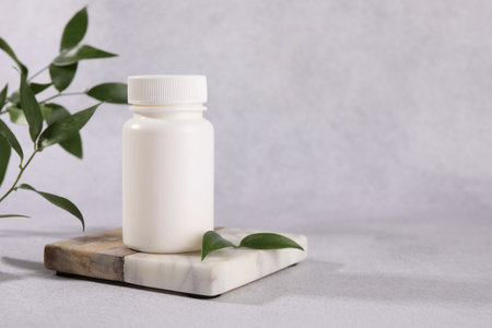 Plastic medical bottle and green leaves on light gray table, space for textの写真素材