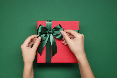 Woman decorating gift box with bow on green background, top viewの写真素材
