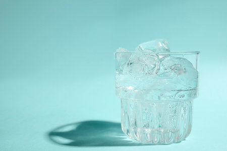 Refreshing water with ice in glass on turquoise background, closeup. Space for textの写真素材