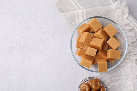 Tasty sweet caramel candies in bowls on light gray table, flat lay. Space for textの写真素材