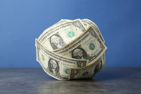 Ball made of dollar banknotes on gray textured table against blue background, closeupの写真素材