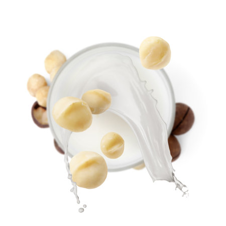 Macadamia nuts falling into glass of milk on white background, top viewの写真素材