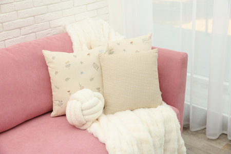 Decorative pillows and fluffy blanket on pink sofa indoors