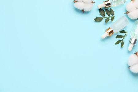 Cosmetic products. Essential oil, leaves and cotton flowers on light blue background, flat lay. Space for textの写真素材