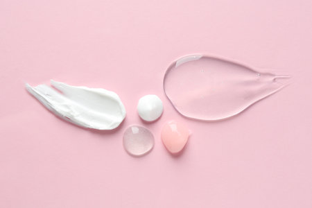 Smears of different cosmetic products on pink background, flat lay