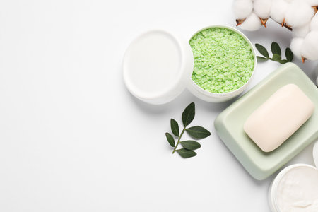 Different cosmetic products, cotton flowers and green leaves on white background, flat lay. Space...