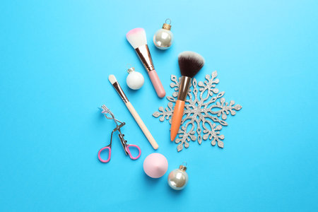 Makeup brushes, eyelash curler and Christmas decor on light blue background, flat layの写真素材