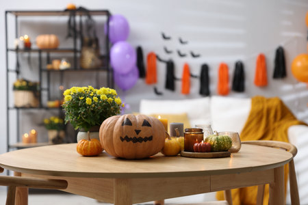 Halloween celebration. Pumpkin with creepy face, candles and flowers on wooden table in decorated roomの写真素材