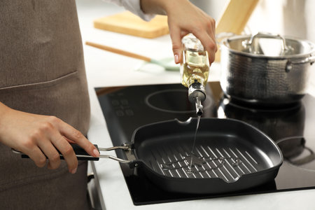 Woman pouring oil into frying pan on cooktop in kitchen, closeupの写真素材