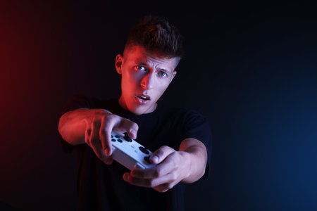 Young man playing video games with controller on black background