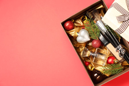 Makeup brushes, cosmetic product, perfume and Christmas decor in box on coral background, top view....