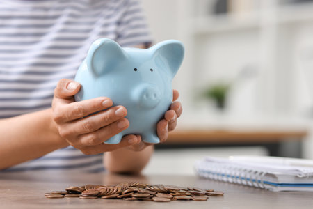Woman holding piggy bank over table with coins indoors, closeupの写真素材