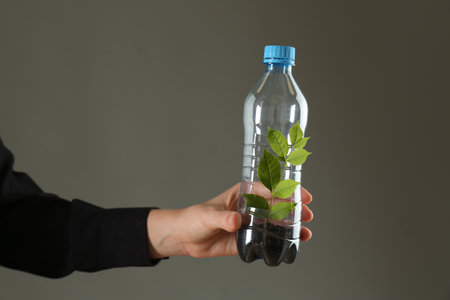 Recycling concept. Woman holding plastic bottle with growing plant against gray background, closeupの写真素材