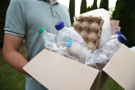 Recycling. Man holding cardboard box with different garbage outdoors, closeupの写真素材