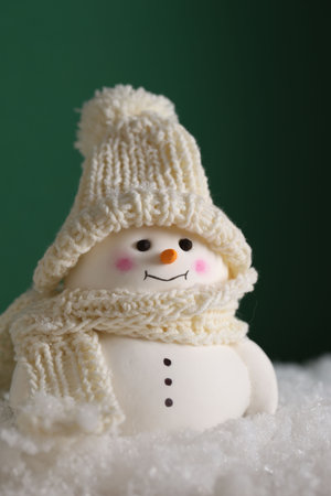 Cute decorative snowman on artificial snow against green backgroundの写真素材