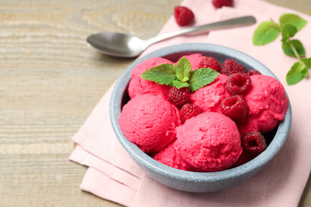 Delicious raspberry sorbet with fresh berries in bowl and spoon on wooden table, closeupの写真素材