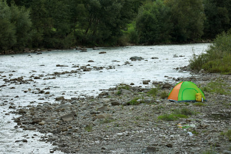 Camping tent, backpack and thermo bottle on stones near river in mountainsの写真素材