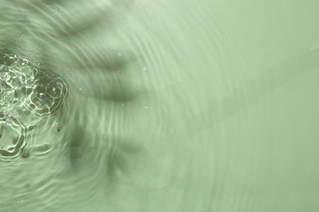 Rippled surface of clear water on light green background, top view