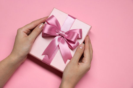 Woman holding gift box with bow on pink background, top viewの写真素材