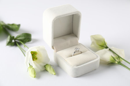 Beautiful ring with gemstone in box and flowers on white background, closeup