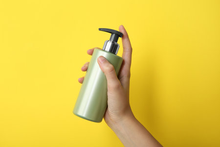 Woman with shampoo bottle on yellow background, closeupの写真素材