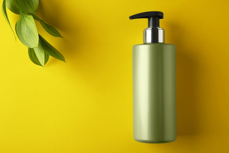Bottle of shampoo and green leaves on yellow background, flat lay. Space for textの写真素材