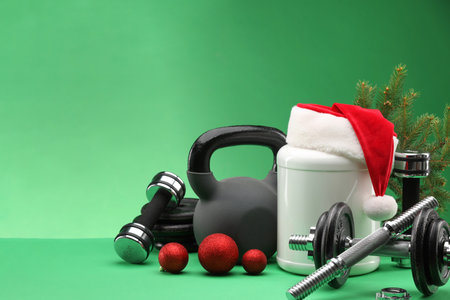 Dumbbells, kettlebell, container with supplement and Christmas decor on green background. Space for textの写真素材