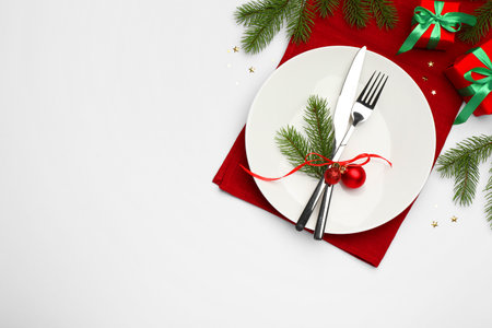 Christmas table setting with plate, cutlery, napkin and festive decor on white background, flat lay. Space for textの写真素材