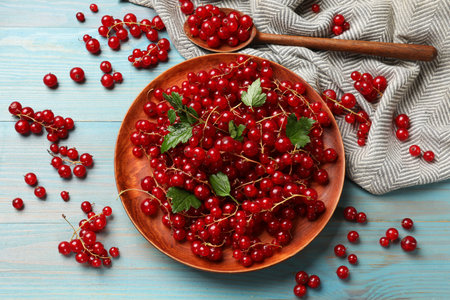 Fresh red currents and leaves on light blue wooden table, flat lay